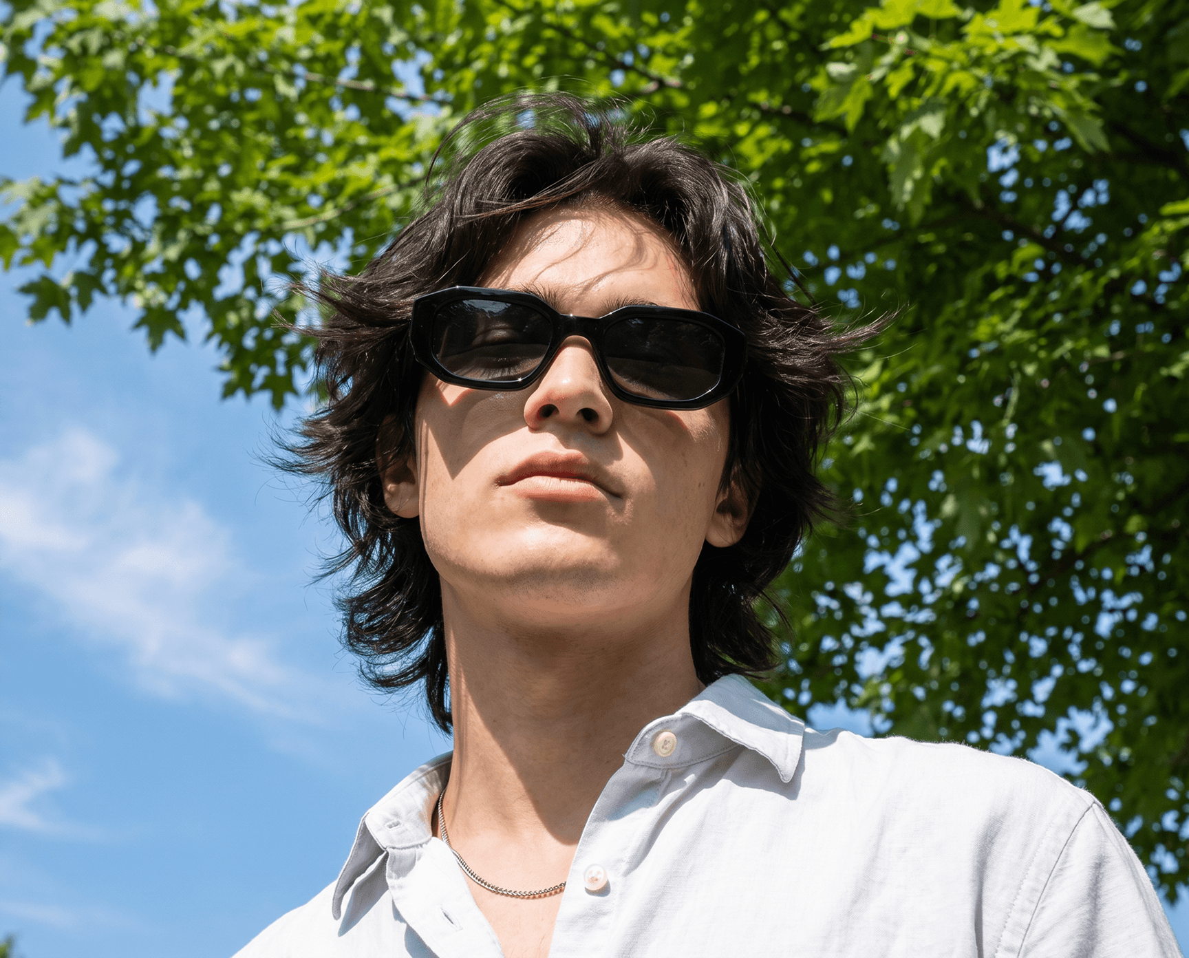 Person wearing sunglasses with a tree and blue sky in the background