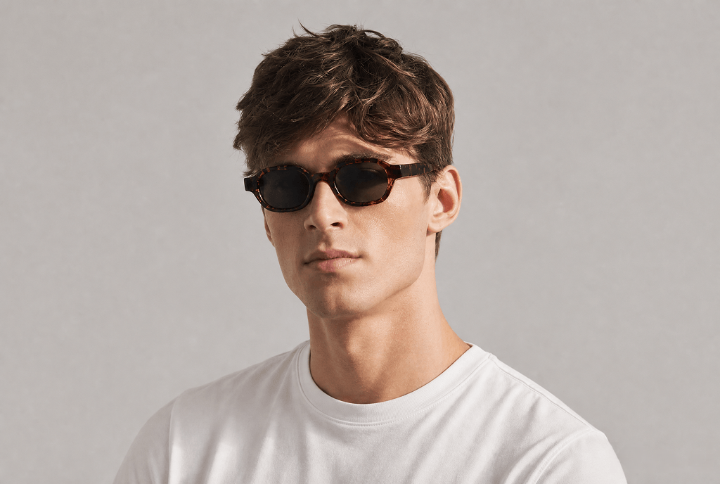Man wearing sunglasses and a white shirt against a gray background tortoiseshell